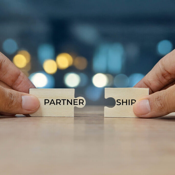 Two hands holding two puzzle pieces to form the word PARTNERSHIP. Collaboration and teamwork concept.